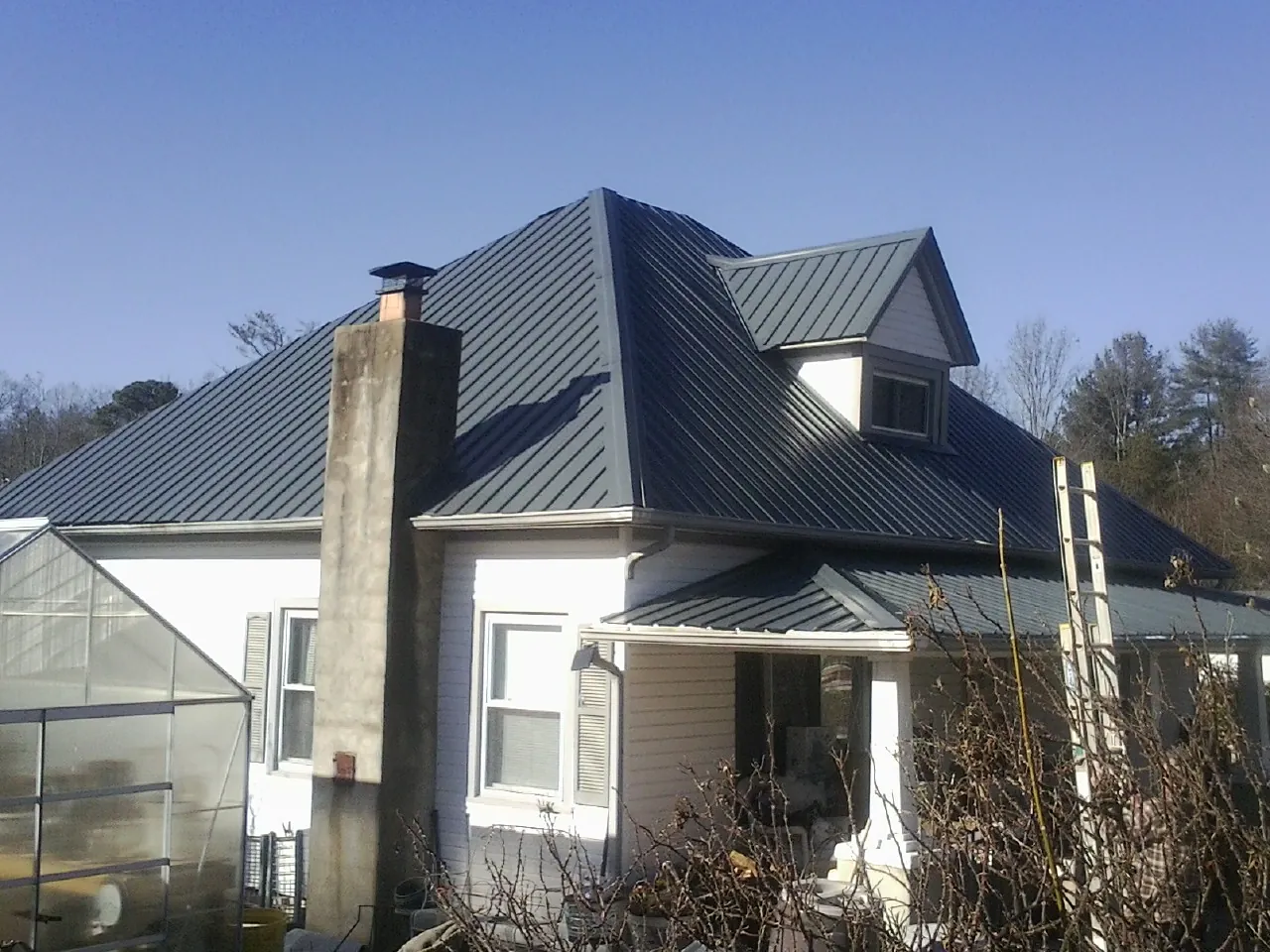 Dark blue standing seam metal roof on a white farmhouse with dormer — Slate & Tile Roof Repair by Roofing Brothers in North Richland Hills