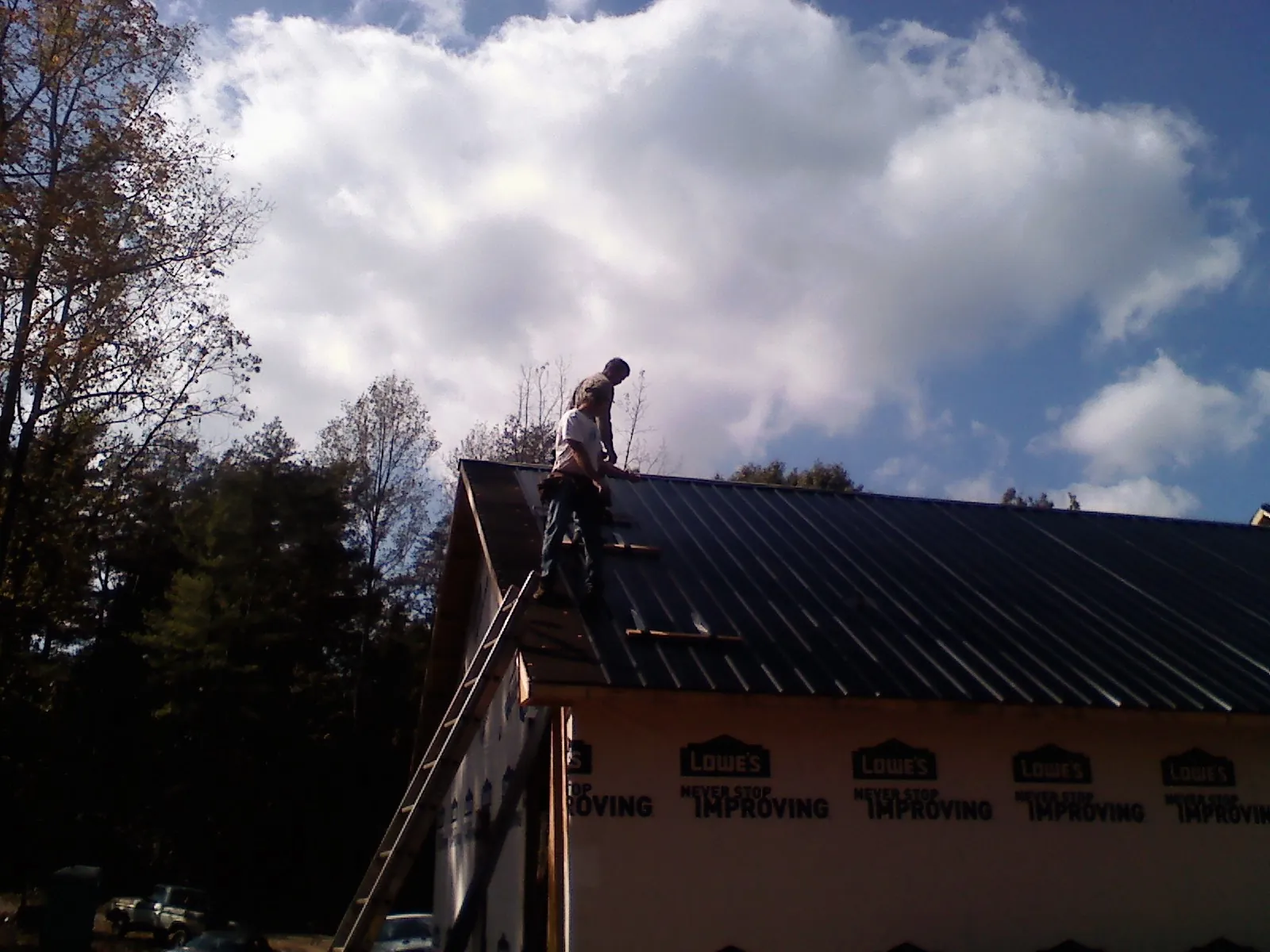 Roofer fastening dark metal panels high against a cloudy sky, from a Roof Inspection job in North Richland Hills