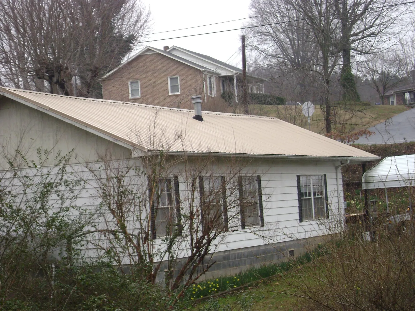 Tan metal roof on a white sided house set into a hillside — Commercial Roofing by Roofing Brothers in North Richland Hills